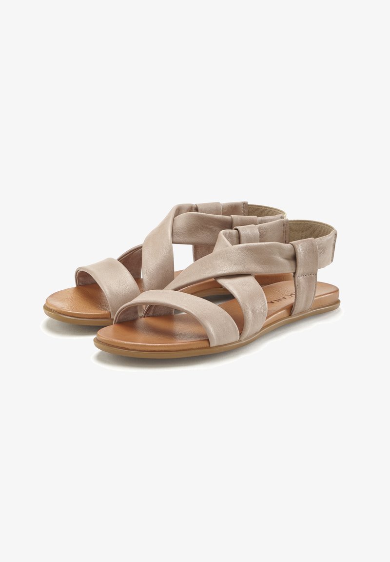 Helle beigefarbene Leder-Sandalen mit überkreuzten Riemen und flacher Sohle. Ausgestattet mit einem braunen Fußbett und einem elastischen Fersenbereich für ein einfaches Anziehen. Glatte Textur.