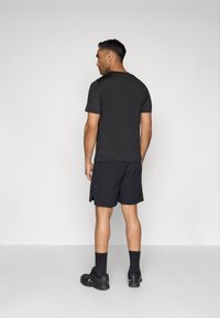 Fekete póló és nadrág készlet, laza szabásban. Texturált anyag, rövid ujjú és látható varrás. A modellen fekete zokni és cipő van.