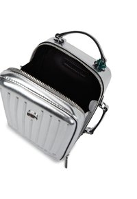 Mała metaliczna, srebrna torebka z górnym uchwytem i zamkiem błyskawicznym, otwarta, aby pokazać czarne materiałowe wnętrze oraz małą wewnętrzną kieszeń.