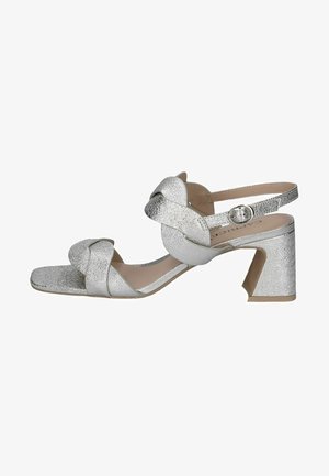 Silver high-heeled sandals featuring a textured finish, a knotted strap design, an open toe, and a chunky heel. Adjustable ankle strap included.