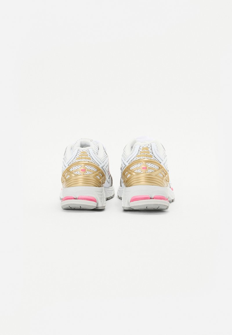 Zapatillas de running blancas con acentos en dorado y rosa, que presentan una parte superior texturizada y paneles de malla. Suela de goma gruesa para soporte y tracción.