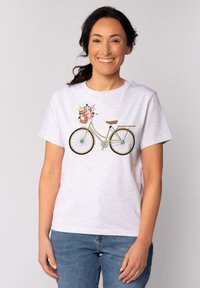 Grijze t-shirt met een fietsafbeelding en een bloemenmand. De fiets is groen met bruine accenten. Model draagt blauwe spijkerbroek.