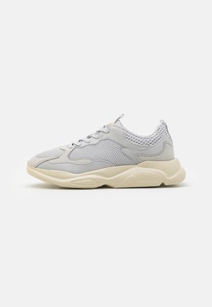 Light grey sneaker with mesh and leather panels, cream thick sole, lace-up closure, and pull tabs on tongue and heel.