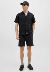 Svart kortärmad skjorta med ett texturerat mönster, parat med matchande svarta shorts. Buren med grå strumpor och mörka skor. Svart keps på huvudet.