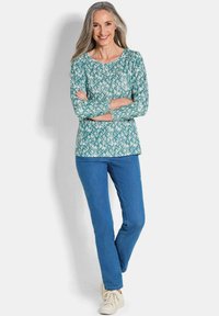 Aqua lange mouw shirt met een geometrisch patroon, gecombineerd met blauwe jeans en lichtgekleurde schoenen. Gladde stof, ontspannen pasvorm, ronde halslijn.