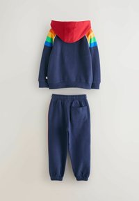 Mørkeblå sweatshirt med rød hætte og regnbuefarvede striber på skuldrene, parret med mørkeblå joggers med elastisk talje og sidelomme.
