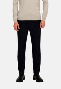 Trousers in dark textured fabric, straight-leg design with a subtle pattern. Paired with black ankle boots and a light-colored sweater.