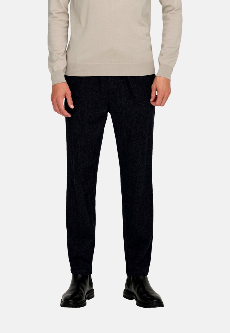 Trousers in dark textured fabric, straight-leg design with a subtle pattern. Paired with black ankle boots and a light-colored sweater.