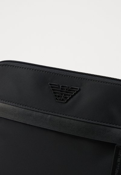 Pochette nera in nylon con accento in pelle testurizzata e logo impresso. Chiusura con zip sulla parte superiore per una conservazione sicura.