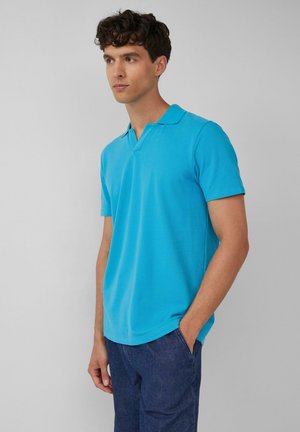 Türkises Poloshirt mit klassischem Kragen, kurzen Ärmeln und lockerer Passform, aus atmungsaktivem Baumwollmaterial, kombiniert mit dunkelblauen Hosen.