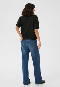 Top nero a maniche corte abbinato a jeans blu larghi con tasche posteriori e design a gamba dritta. Tessuto texture visibile.