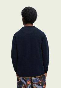 Marineblauwe gebreide trui met een ronde halslijn en geribbelde manchetten, gecombineerd met gestreepte shorts in felle kleuren en abstracte ontwerpen.