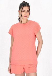 Koralfarvet quilted bomulds t-shirt med korte ærmer og rund halsudskæring, parret med matchende shorts, begge med en tekstureret overflade.