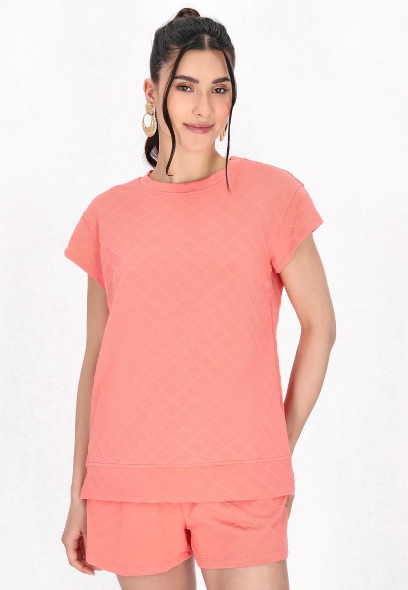 Koralfarvet quilted bomulds t-shirt med korte ærmer og rund halsudskæring, parret med matchende shorts, begge med en tekstureret overflade.