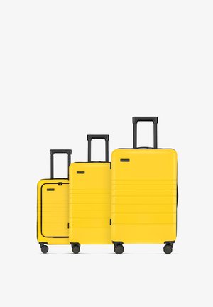 Drei gelbe Hartschalenkoffer in unterschiedlichen Größen verfügen über horizontale Linien, schwarze Griffe und Räder für eine einfache Handhabung.