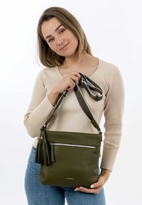Olive green leather crossbody bag with textured surface, featuring a front zip pocket and decorative tassel, with a gray adjustable strap.