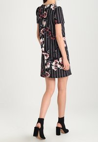 Kortärmad svart klänning med vertikala ränder och blommönster i nyanser av rosa. Har en rak skärning och är styling med ankelstövlar.