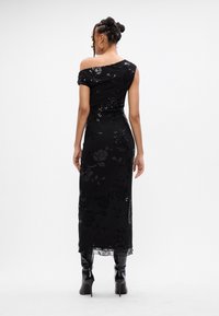 Melnas, ārpus pleca valkājamas kleitas ar ziedu rakstu un spīdīgām akcentēm, ar pieguļošu siluetu un midi garumu. Stilizēta ar ceļgala augstuma zābakiem.