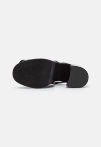 Semelle noire d'une chaussure à talon bas avec semelle avant texturée et talon lisse, vue de dessous sur un fond blanc uni.