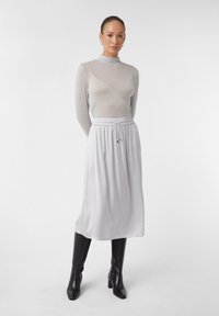 Haut gris clair à manches longues avec un col montant, associé à une jupe fluide longueur cheville de couleur gris clair. Bottes noires à talons, hauteur genou.