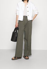 White cropped button-up jacket, beige top, olive green wide-leg trousers, black bucket bag, and black platform sandals.