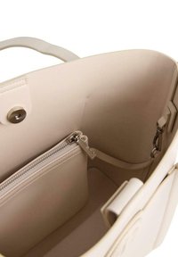 Interno di una borsa a tracolla in pelle beige con una tasca con zip, texture liscia e chiusura a scatto. Include cuciture interne e dettagli in metallo.