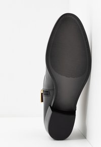 Semelle de chaussure habillée en cuir noir avec une texture antidérapante et un petit talon empilé, montrant une fermeture éclair dorée sur le côté.