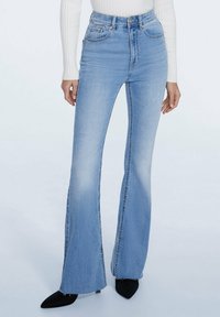 Hoge taille flared jeans in lichtblauwe denim met een vervaagde was, vijf zakken en een rafelrand, gecombineerd met zwarte puntige hakken.