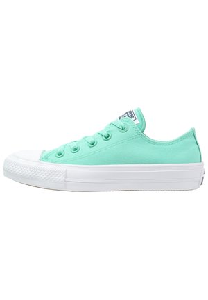 Zapatilla deportiva de lona verde claro de corte bajo con suela y puntera de goma blanca, cordones verdes a juego y parche con logo en la lengüeta.
