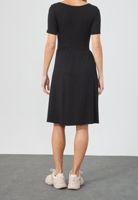 Černé krátké šaty s přiléhavým živůtkem a rozšířenou sukní. Hladká látka, délka po kolena, nošeny s světle zbarvenými teniskami.