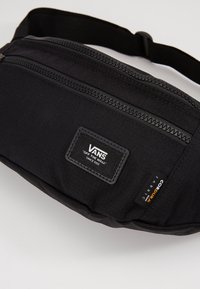 Sac banane noir en tissu durable, avec un compartiment zippé, un patch logo Vans et une étiquette en tissu Cordura.
