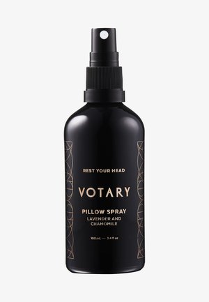 Sort flaske med spraydyse, prydet med guldtekst. Etiket angiver "Votary Pude Spray Lavendel og Kamille," med en kapacitet på 100 mL.