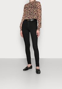 Blusa floreale con base nera e fiori multicolori, abbinata a jeans skinny neri a vita alta e mocassini neri con dettagli in oro.