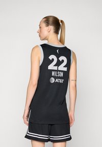 Maillot de basket-ball noir avec des accents gris, numéro 22, et "WILSON" au dos. Texture en maille et logo AT&T affiché. Stylé avec un short noir.