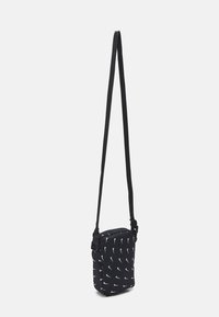 Černá crossbody taška z látky, s zipovým zavíráním, nastavitelným popruhem a opakujícím se vzorem bílého loga. Kompaktní obdélníkový tvar.