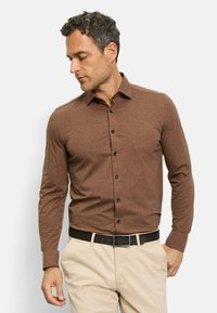 Braun langärmliges Hemd mit Button-Down-Kragen, ausgestattet mit schwarzen Knöpfen und glattem Stoff, kombiniert mit hellbeigen Hosen und einem dunklen Gürtel.