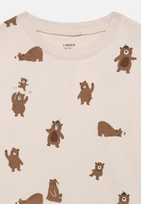 Beige bomulds T-shirt med et mønster af brune tegneserie-bjørne i forskellige positurer, hvoraf nogle har hatte på, med rund hals og korte ærmer.