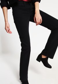 Schwarze, weit geschnittene Jeans aus Denim mit einem klassischen Fünf-Taschen-Design und dezenten Nähten. Getragen mit schwarzen Knöchelstiefeln.