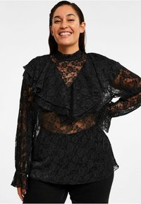 Sort blonde bluse med rynket halsudskæring og gennemsigtige ærmer, med et tekstureret skørt og blomsterprint over det hele.