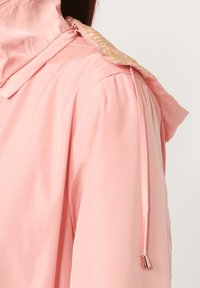 Chaqueta ligera rosa con textura brillante y suave. Cuenta con un collar estampado y un cordón ajustable en el hombro.