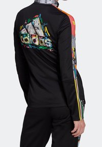 Long-sleeve black athletic top with colorful multi-patterned accents and a prominent graphic logo on the back. Features contrasting side stripes.