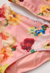 Bikini sæt med blomsterprint på en pink baggrund med flerfarvede blomster. Trusserne har en bølget kant. Fremstillet af blødt, elastisk stof.