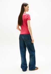 Camiseta ajustada rosa de manga corta combinada con jeans azul holgados que cuentan con bolsillos traseros y una textura suave.