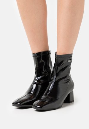 Zwarte lakleren enkellaarsjes met een vierkante neus, blokhak en een gladde glanzende afwerking, voorzien van een zijrits en een hakhoogte van ongeveer 5 cm.