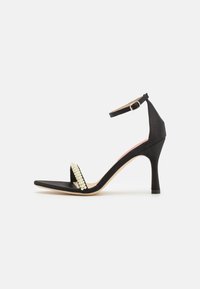 Black suede high-heeled sandals with ankle strap, square toe, and rhinestone embellishment across the front.