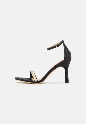 Fekete velúr magassarkú szandál, bokapánttal, négyzetes orral és strasszkövekkel díszített elülső résszel.