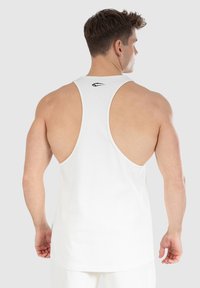 Biała bezrękawnikowa koszulka z plecami typu racerback, z małym czarnym logo z tyłu, wykonana z lekkiej tkaniny bawełnianej.