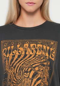 Zwarte katoen t-shirt met een oranje skeletgrafiek, omringd door draaikolken en vintage typografie. Ronde halslijn en korte mouwen.