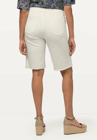 Bermudas de algodón blancas con dobladillo sin terminar, con bolsillos traseros. Combinadas con sandalias de cuña beige y una blusa de estampado.