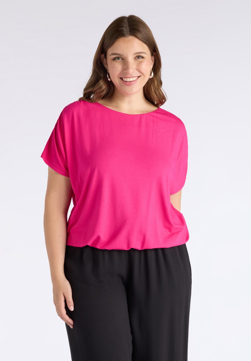 Top rosa de manga corta con corte holgado y escote ancho, combinado con pantalones negros de talle suelto. Tela suave con un ligero brillo.
